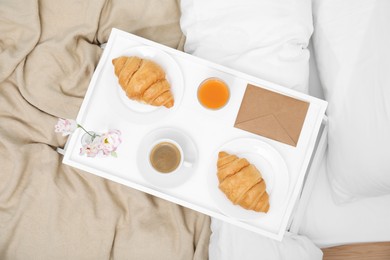 Tray with tasty croissants, drinks and flowers on bed, top view