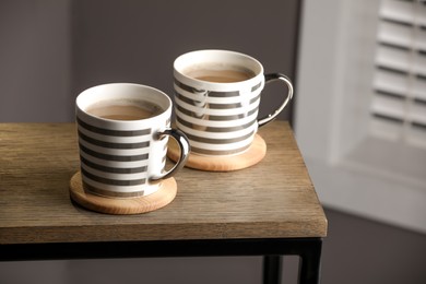 Photo of Mugs of coffee with stylish cup coasters on wooden table in room