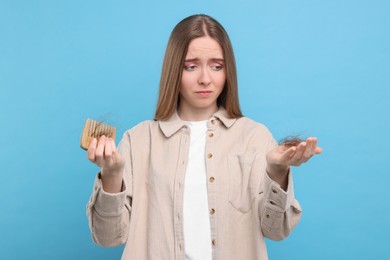Photo of Upset woman holding comb with lost hair on light blue background. Alopecia problem