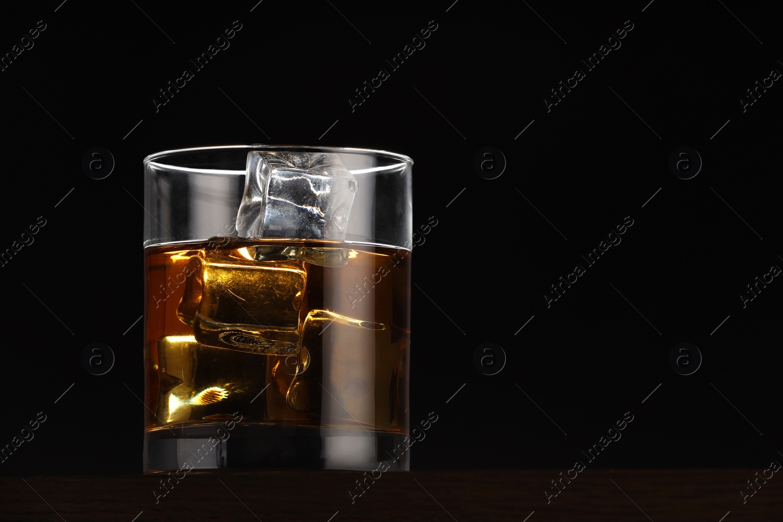 Photo of Whiskey with ice cubes in glass on table against black background. Space for text