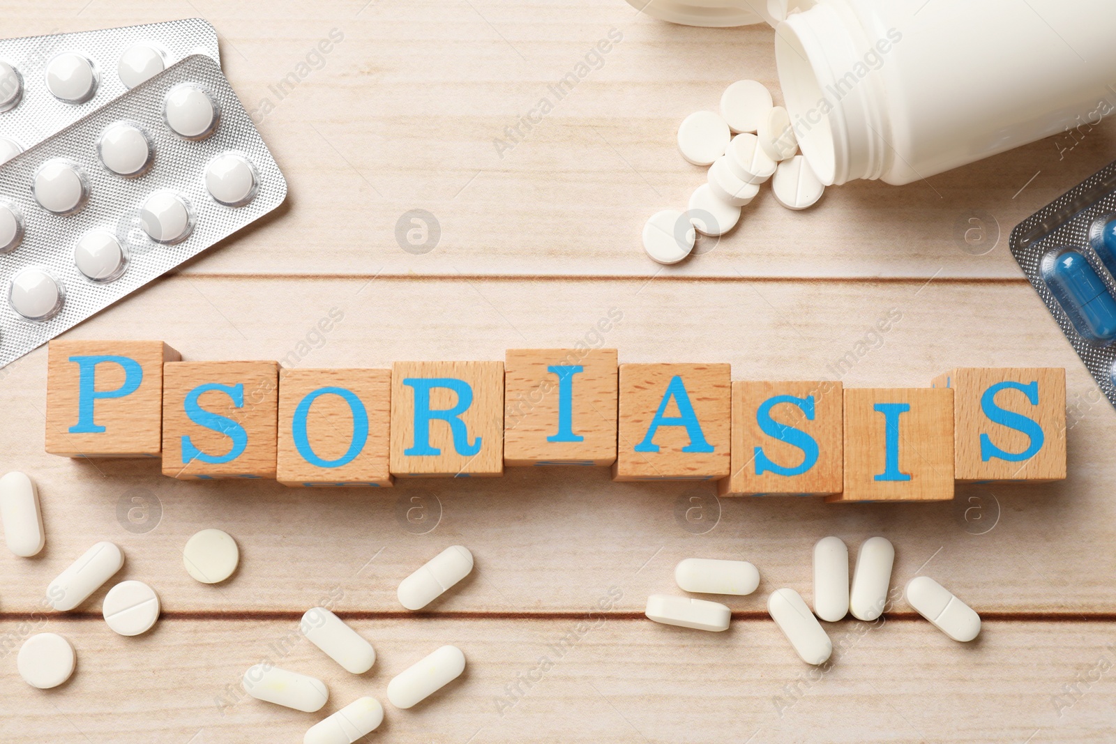 Photo of Word Psoriasis made of cubes with letters and pills on wooden table, flat lay