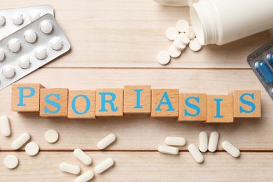 Photo of Word Psoriasis made of cubes with letters and pills on wooden table, flat lay