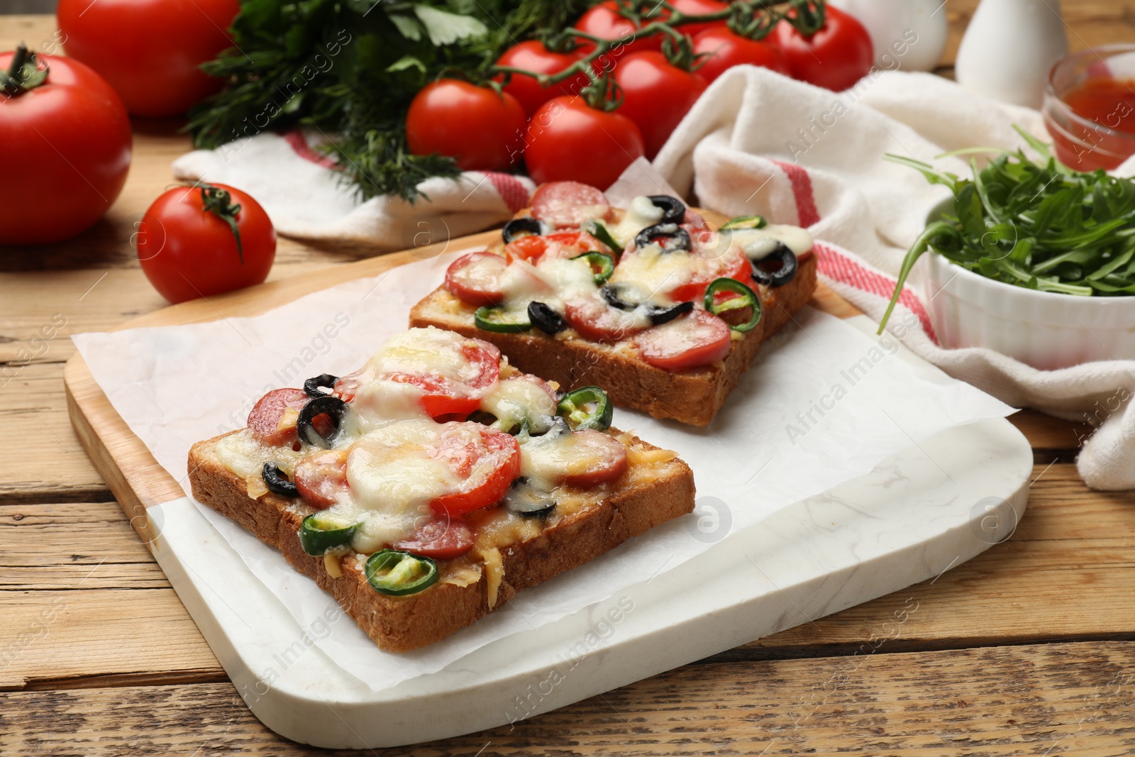 Photo of Tasty pizza toasts, arugula and tomatoes on wooden table