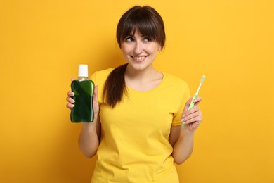 Young woman with mouthwash and toothbrush on yellow background