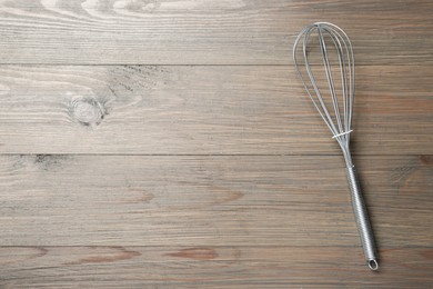 One metal whisk on wooden table, top view. Space for text