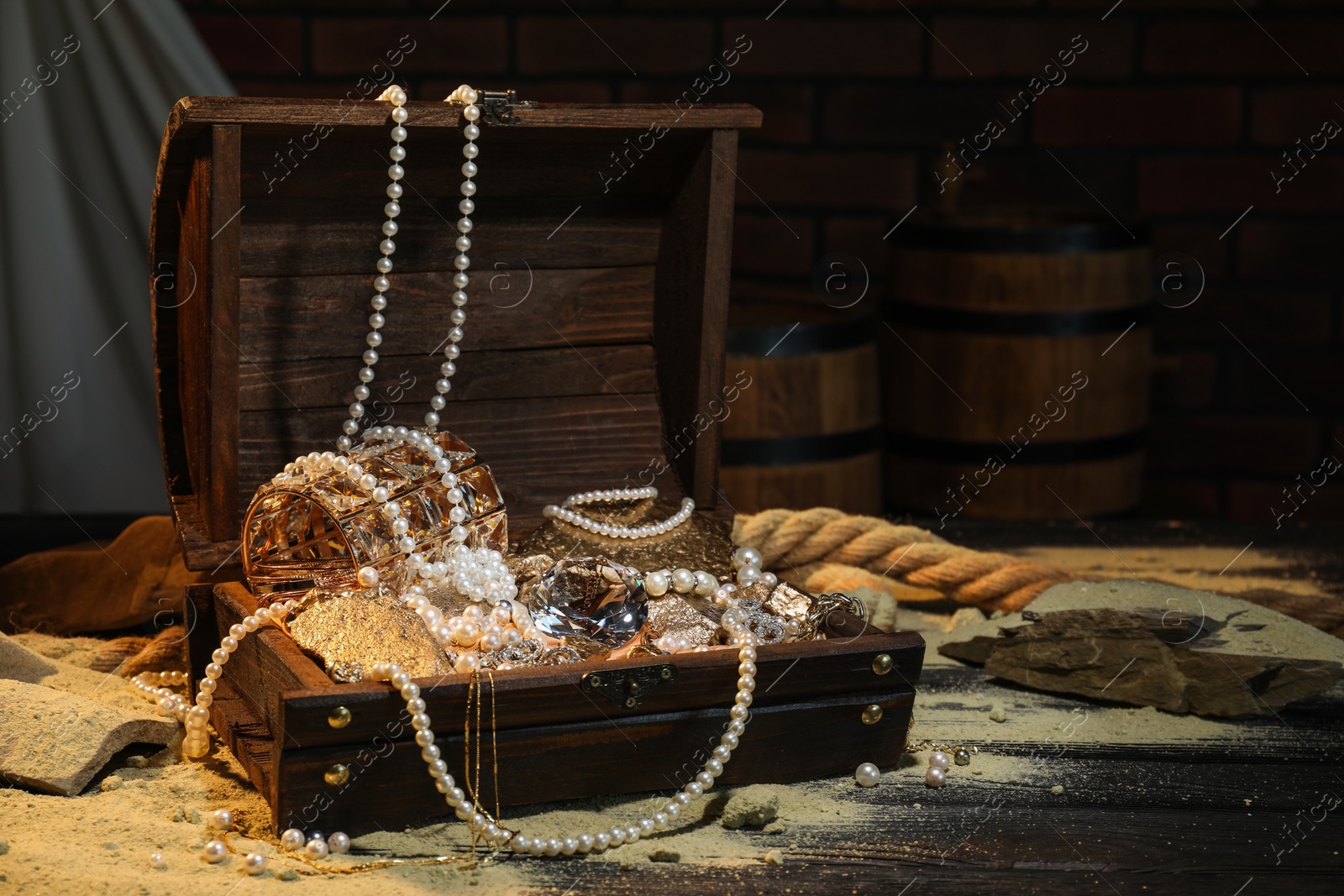 Photo of Chest with treasures and scattered sand on wooden table, space for text