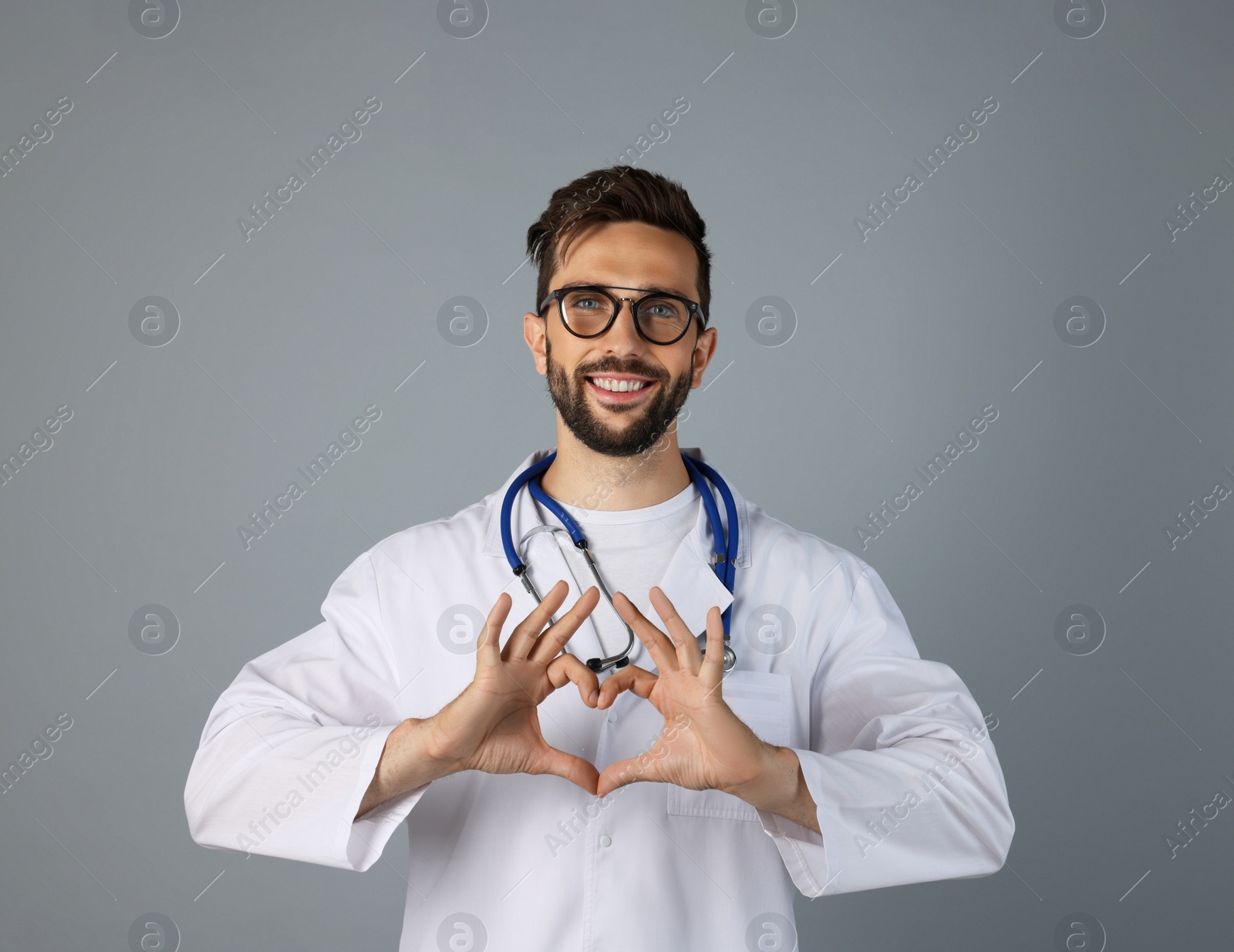 Photo of Doctor making heart with hands on grey background