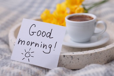 Photo of Cup of coffee, flowers and card with phrase GOOD MORNING! on knitted paid, closeup