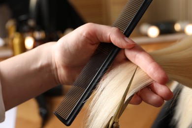 Photo of Hairdresser cutting client's hair with scissors in salon, closeup