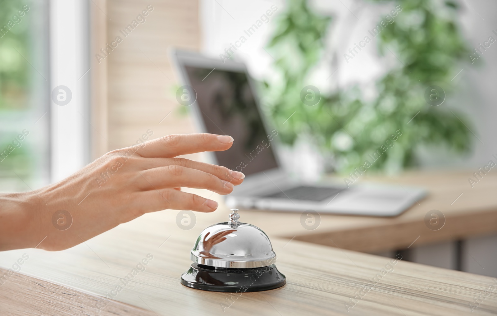 Photo of Woman ringing service bell on reception desk in hotel, closeup