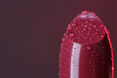 Beautiful red lipstick with water drops on brown background, macro view. Space for text