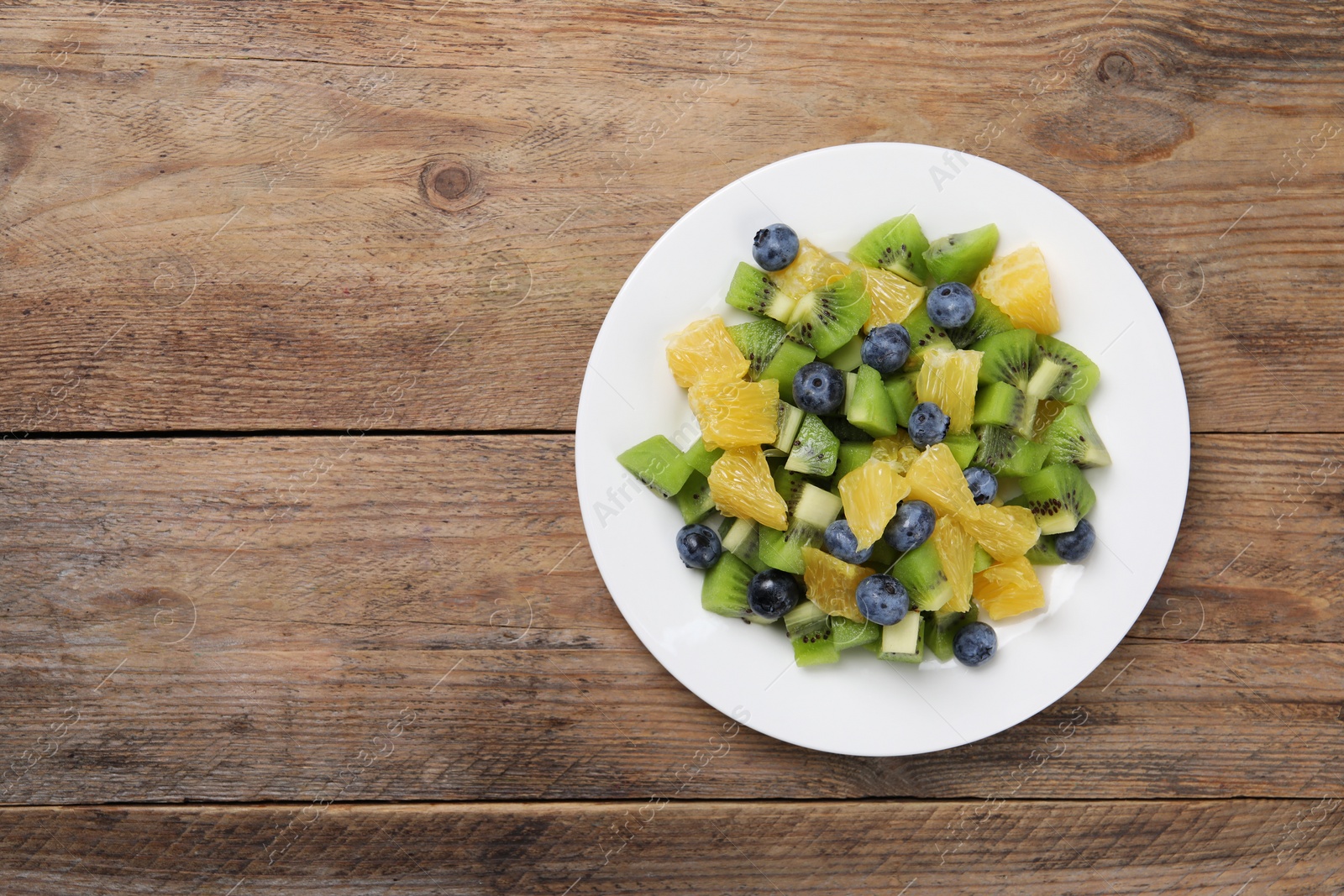 Photo of Plate of tasty fruit salad on wooden table, top view. Space for text