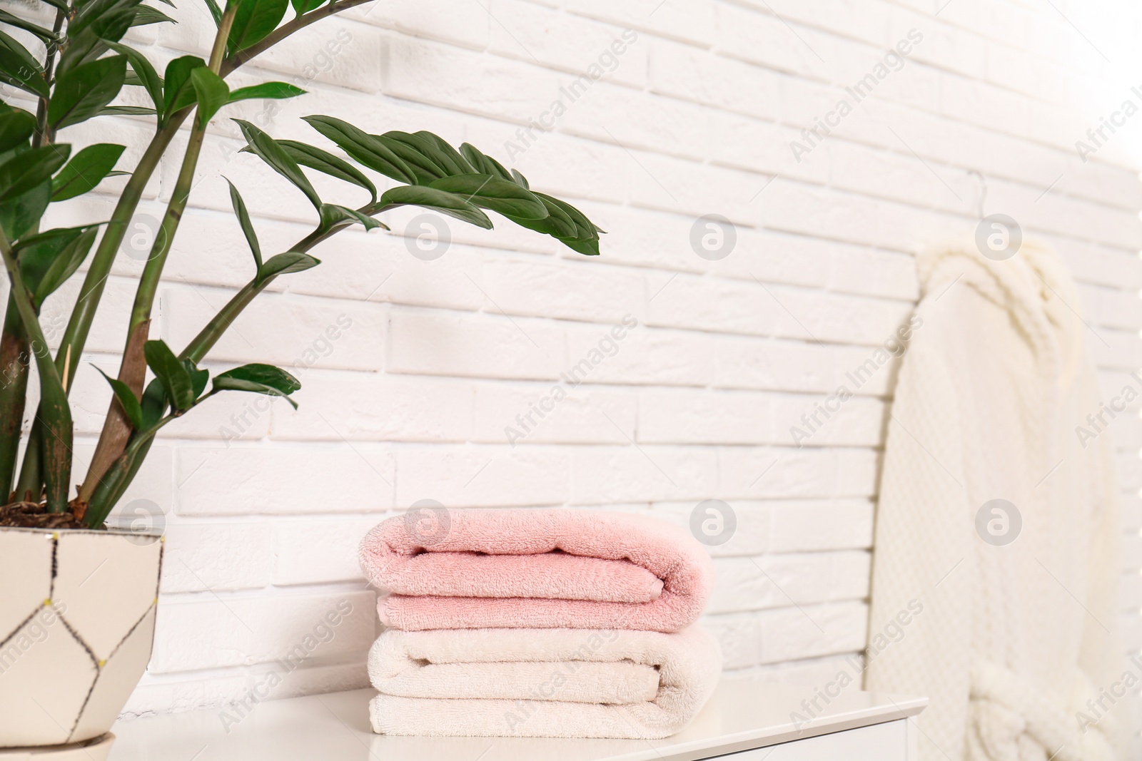 Photo of Clean folded towels on table near brick wall. Space for text