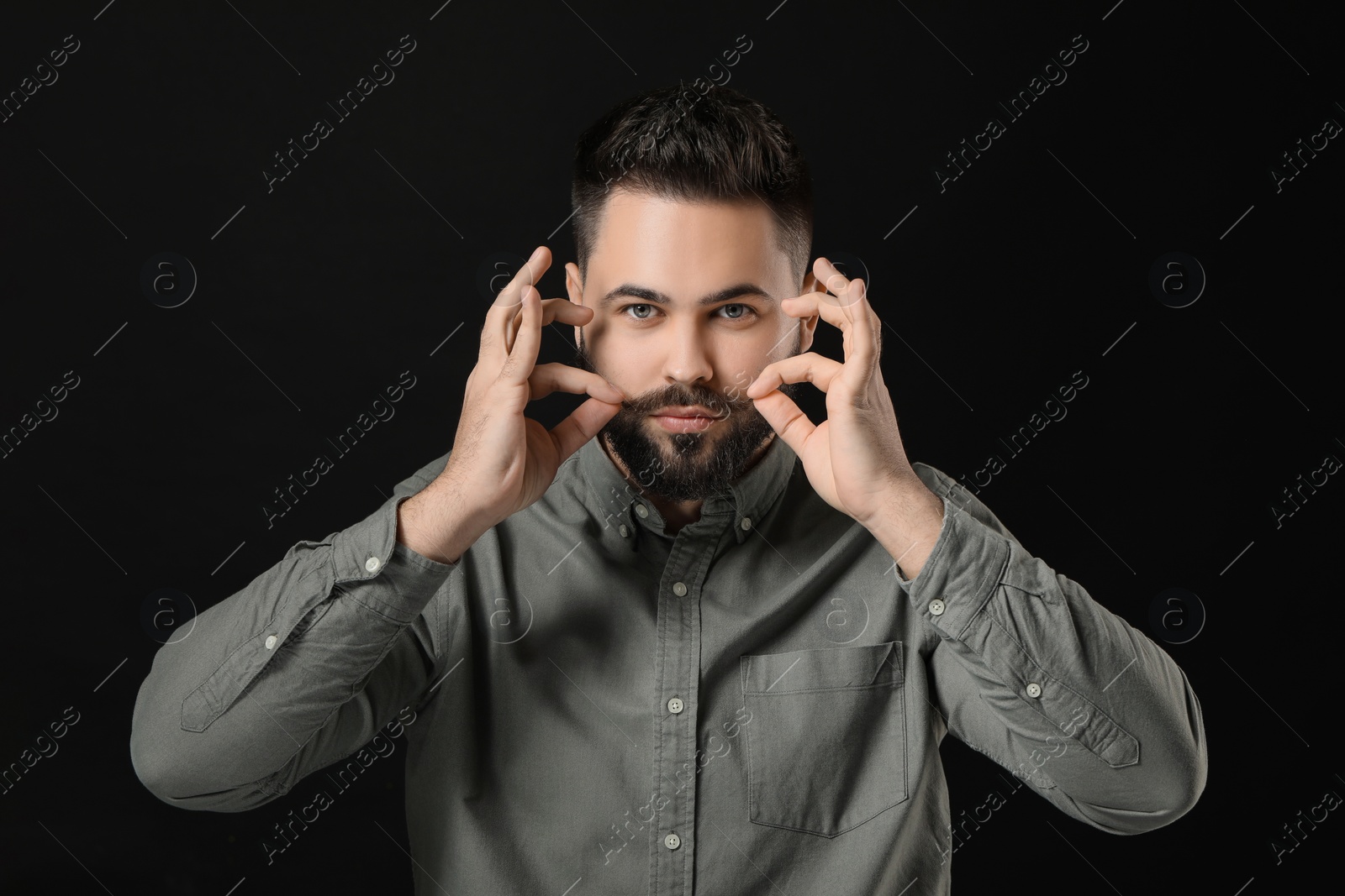 Photo of Young man in shirt touching mustache on black background
