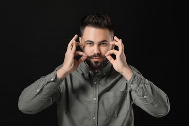 Young man in shirt touching mustache on black background