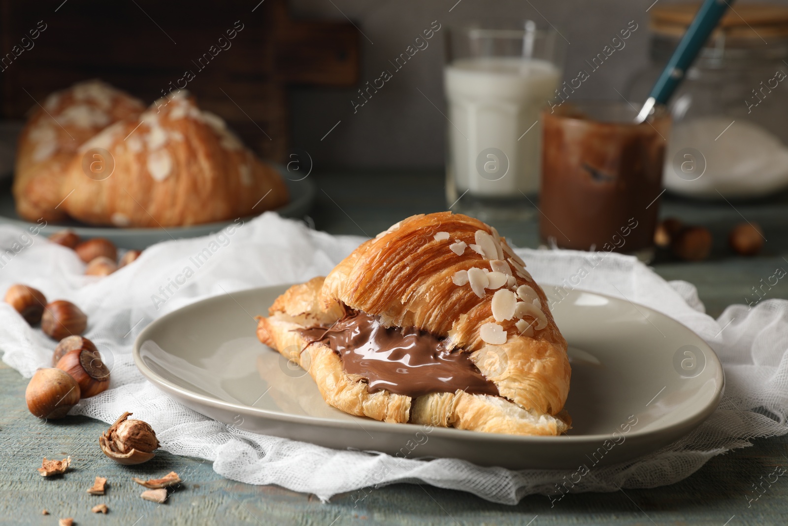 Photo of Delicious croissant with chocolate and nuts on light blue wooden table