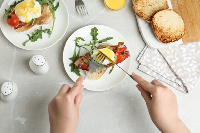 Woman eating tasty egg Benedict at light grey marble table, top view