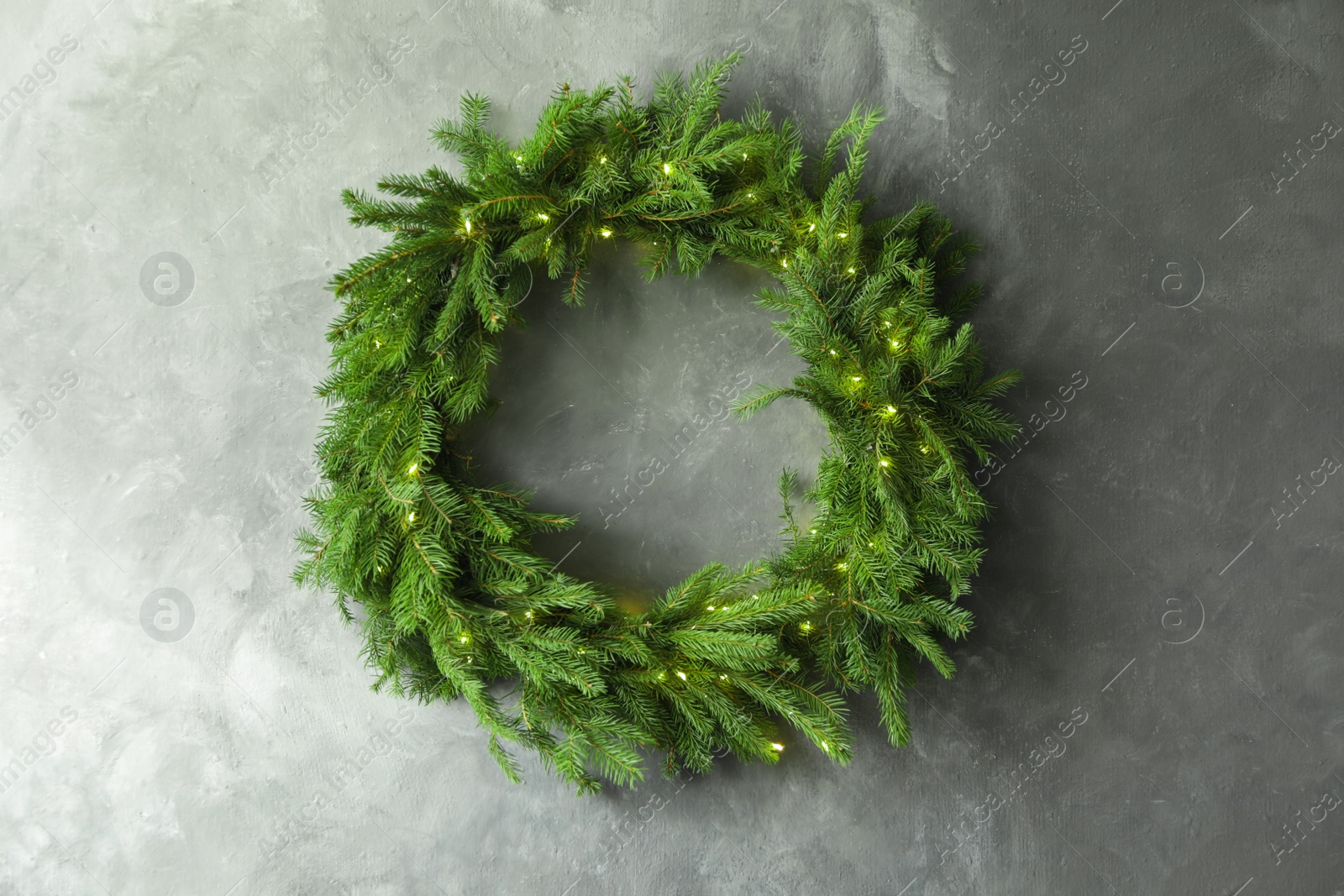 Photo of Beautiful Christmas wreath with festive lights on grey wall