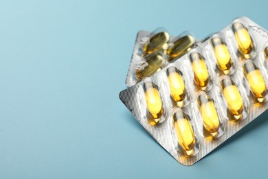 Photo of Dietary supplement capsules in blister packs on light blue background, closeup. Space for text