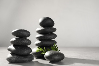 Stacks of spa stones and green leaves on grey table, space for text