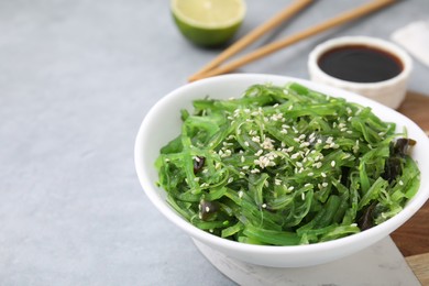 Photo of Tasty seaweed salad in bowl served on gray table, closeup. Space for text