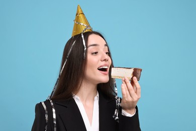 Photo of Woman in party hat eating piece of tasty cake on light blue background