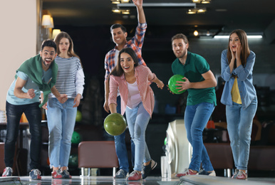 Young woman throwing ball and spending time with friends in bowling club