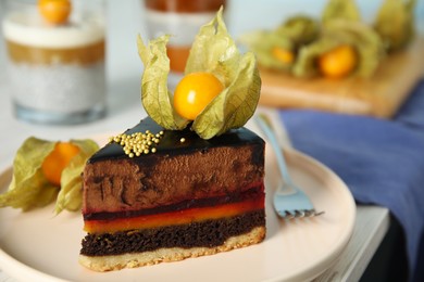 Photo of Piece of tasty cake decorated with physalis fruit on white wooden table, closeup