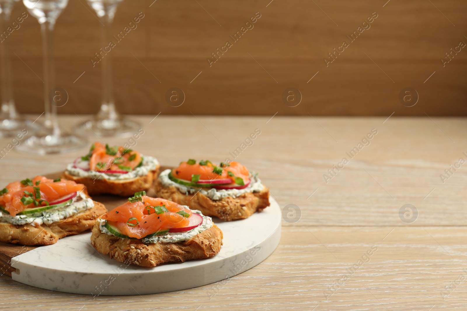 Photo of Tasty canapes with salmon, cucumber, radish and cream cheese on wooden table, space for text