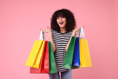 Happy young woman with shopping bags on pink background