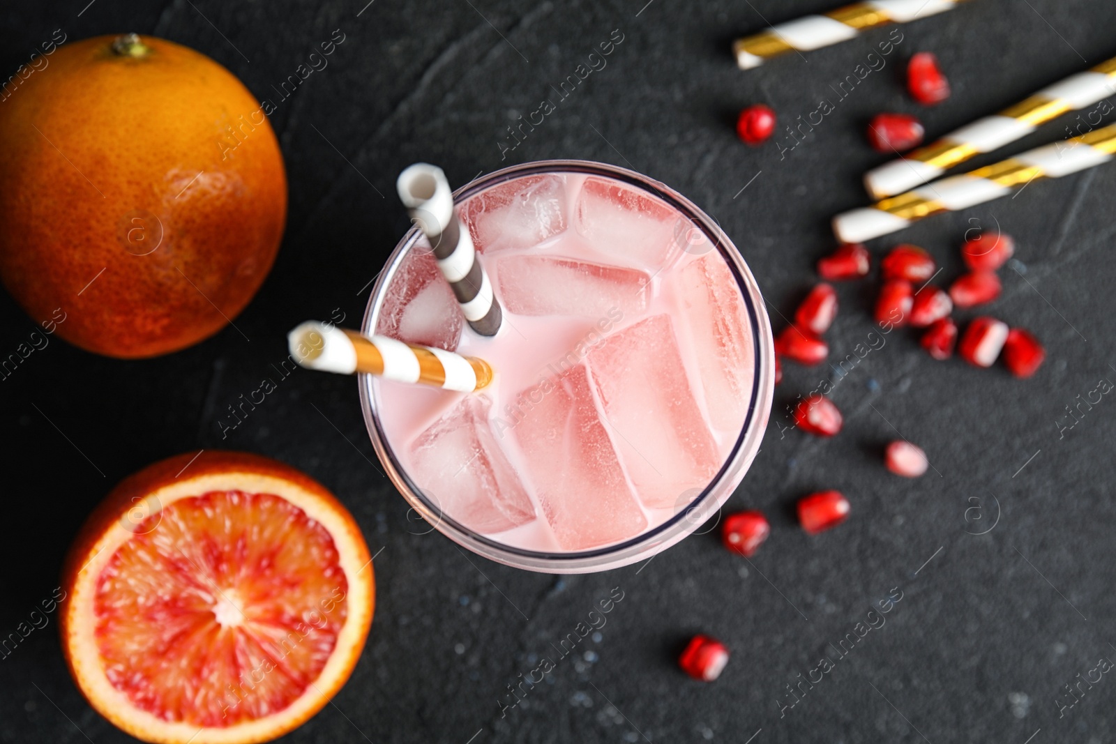 Photo of Glass of tropical cocktail with ice cubes and fruit on black background, flat lay