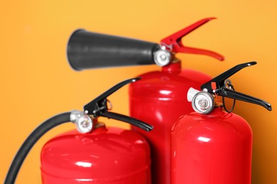 Three red fire extinguishers on orange background, closeup