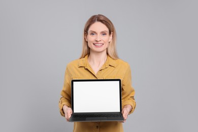 Happy woman showing laptop on light grey background