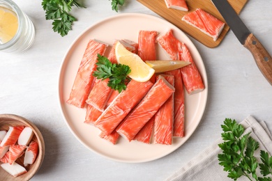 Flat lay composition with crab sticks, lemon, parsley and knife on white table