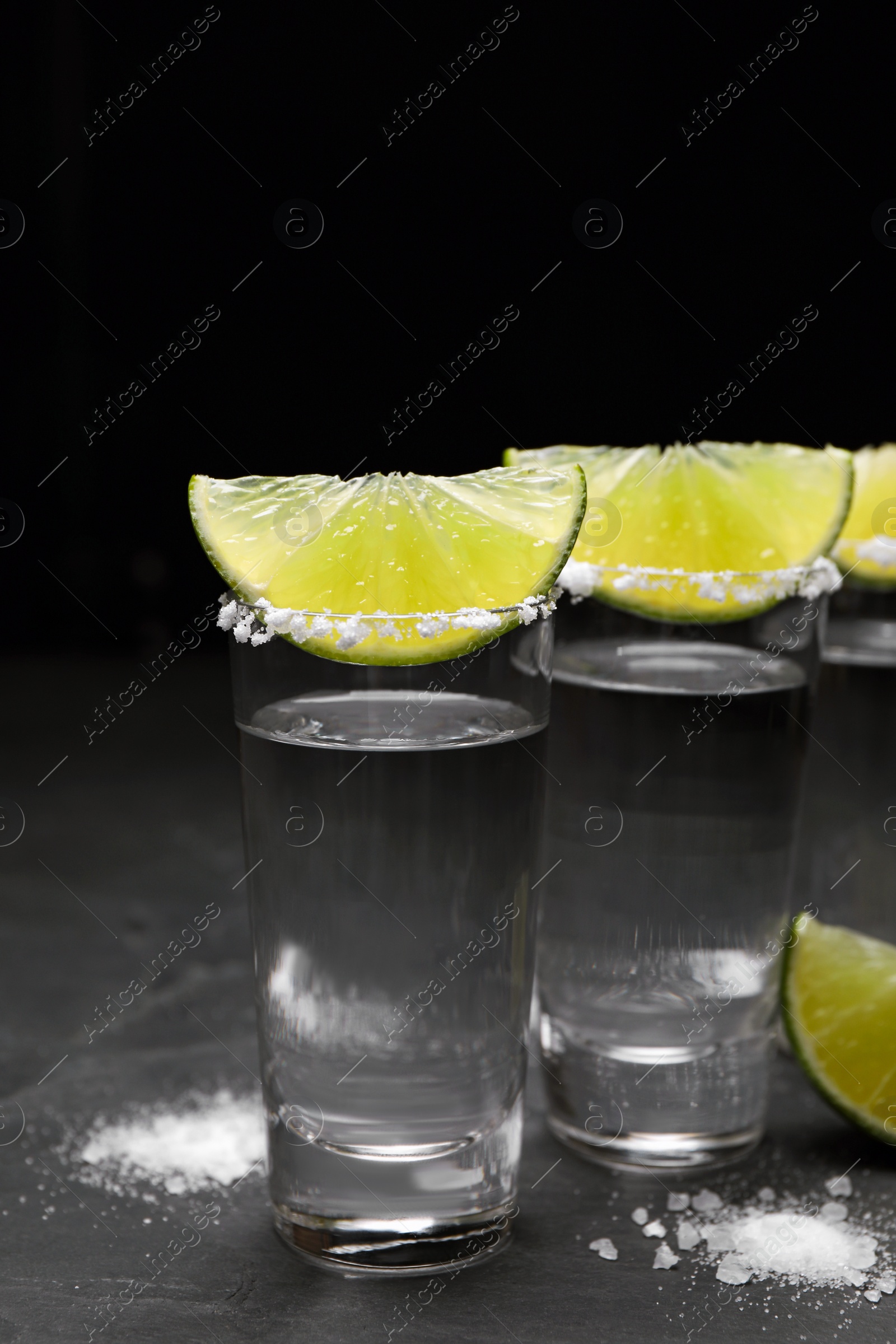 Photo of Mexican Tequila shots, lime slices and salt on black table