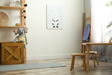 Photo of Cute picture on white wall and wooden furniture indoors. Children's room interior design