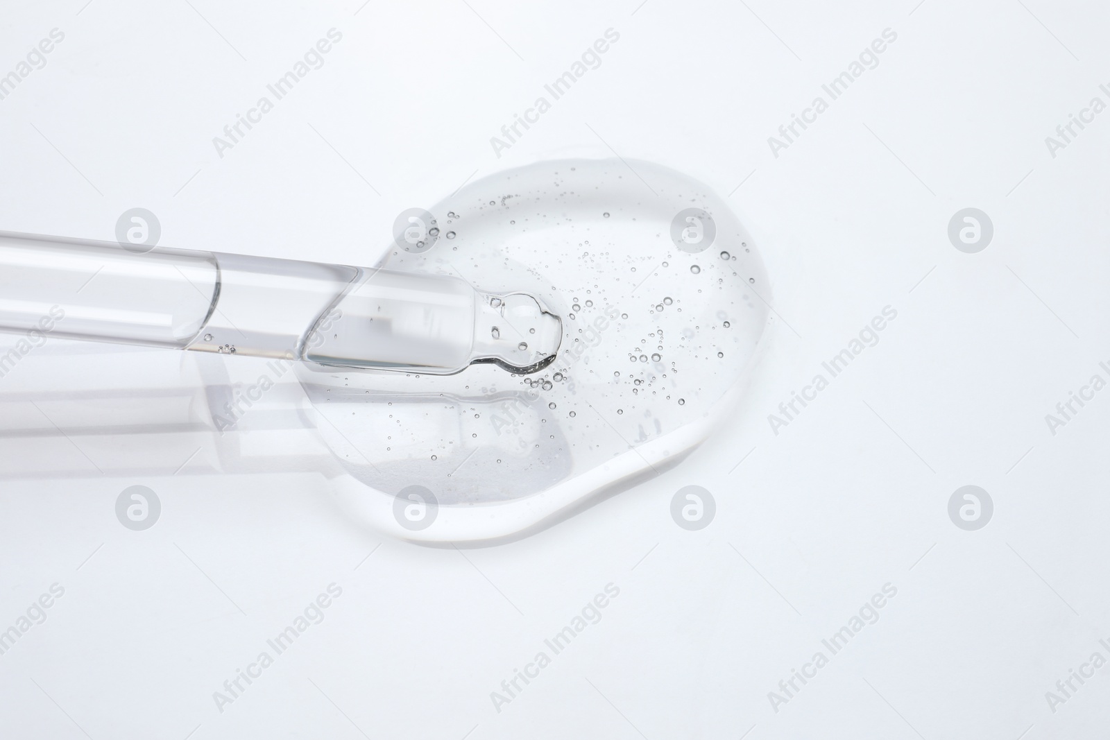 Photo of Dripping cosmetic oil from pipette onto light surface, closeup