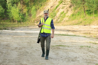 Photo of Man with hunting rifle wearing safety vest outdoors