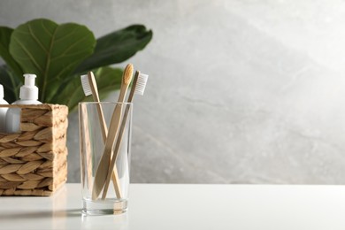 Photo of Bamboo toothbrushes in glass holder and cosmetic products on white countertop, space for text