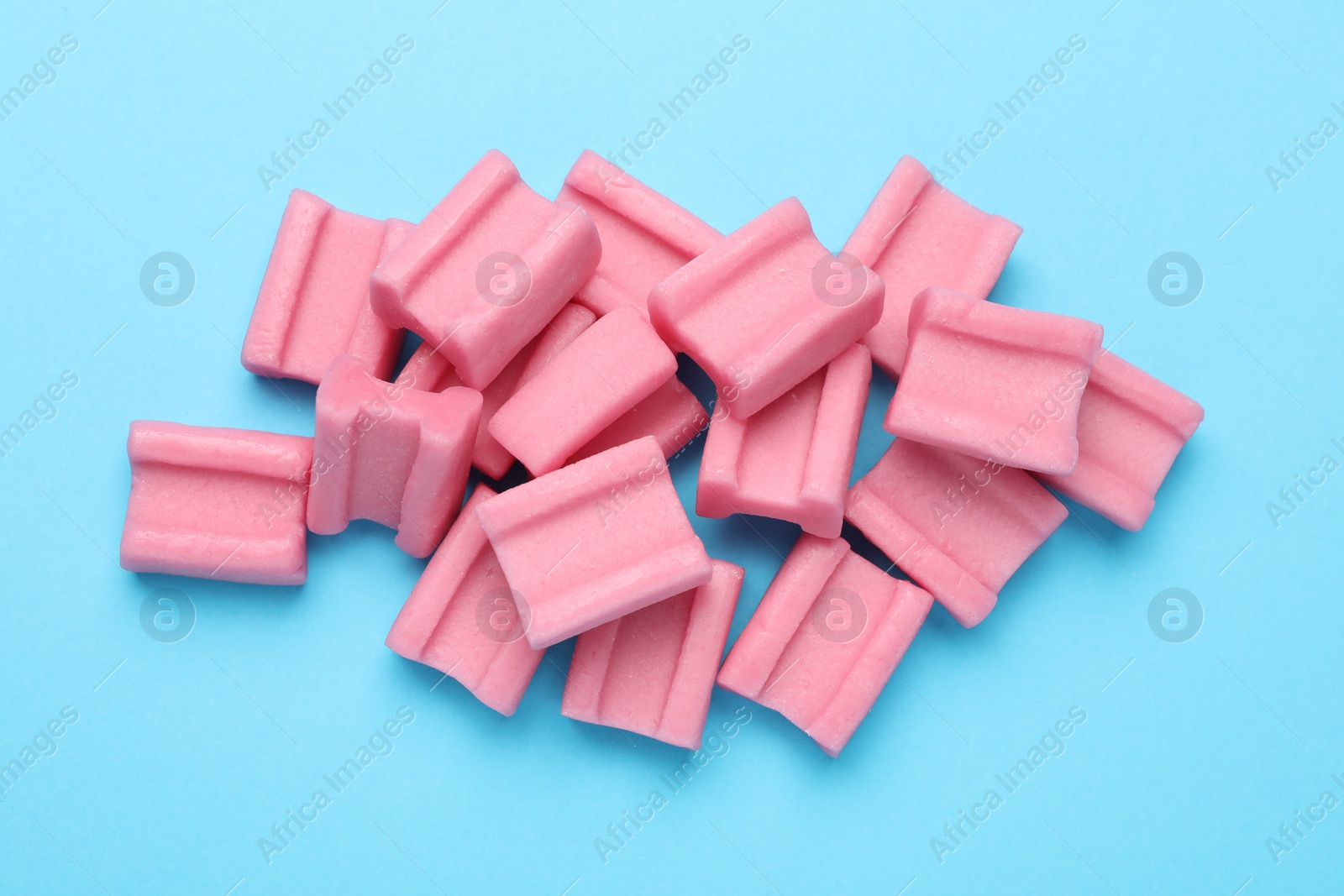 Photo of Tasty pink chewing gums on light blue background, flat lay