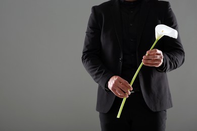 Photo of Man with calla lily flower on grey background, closeup and space for text. Funeral ceremony