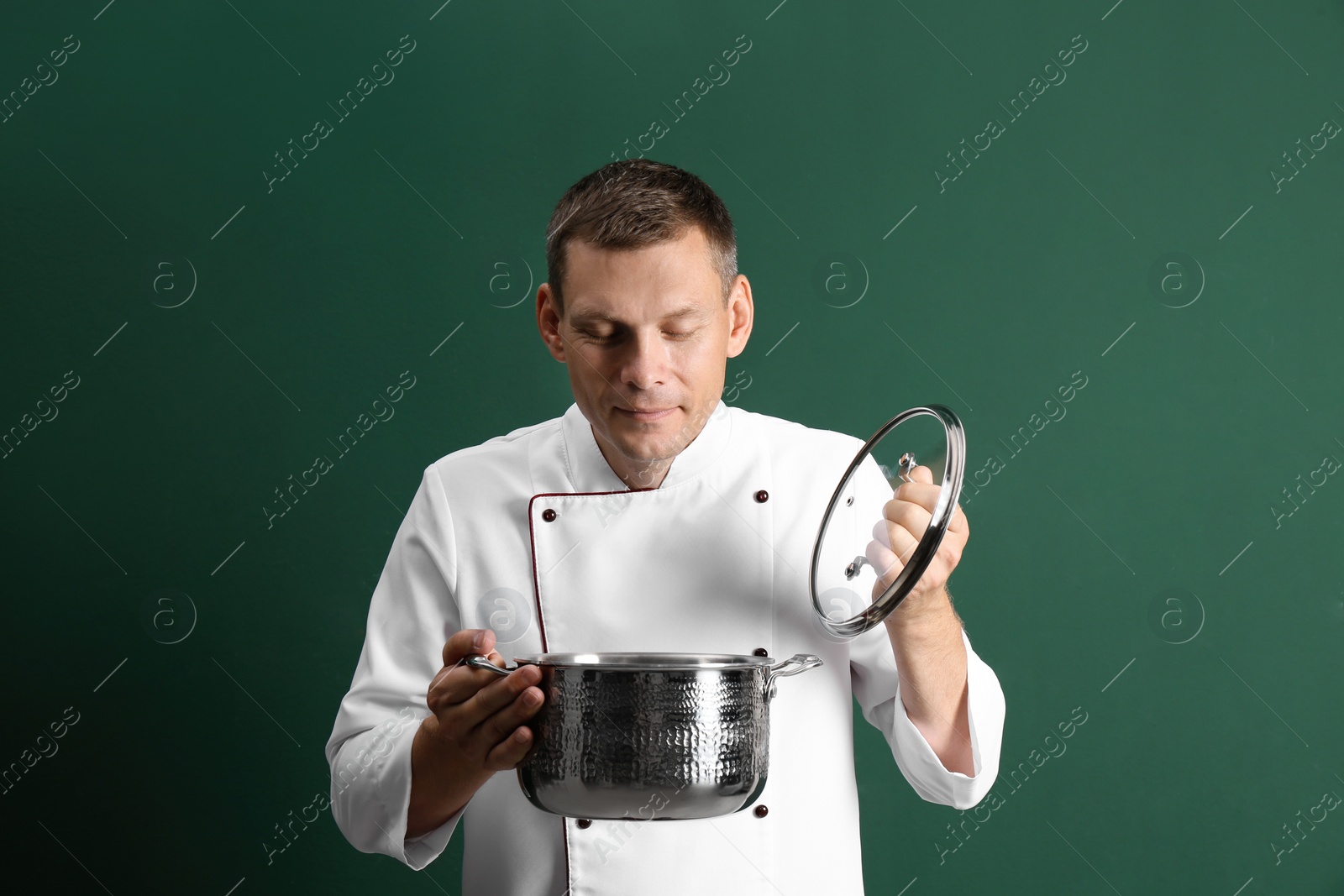 Photo of Happy male chef with cooking pot on dark green background