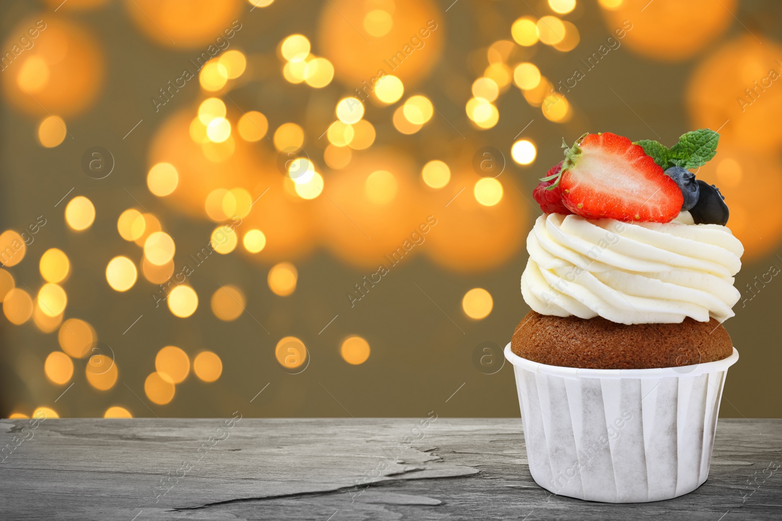 Image of Sweet birthday cupcake with fresh berries on black table against blurred lights. Space for text