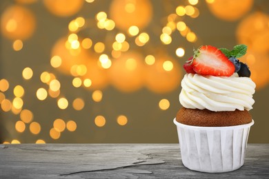 Image of Sweet birthday cupcake with fresh berries on black table against blurred lights. Space for text