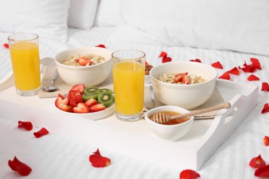 Photo of Tray with tasty breakfast and rose petals on bed at home