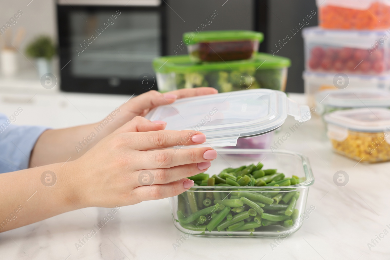 Photo of Woman sealing container with green beans at white marble table in kitchen, closeup. Food storage