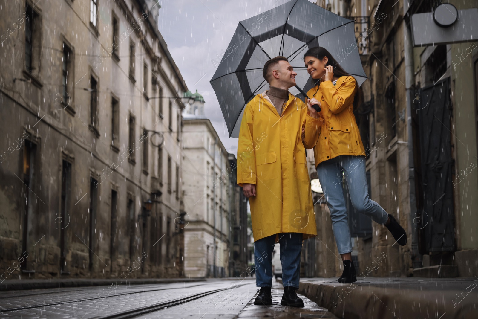 Photo of Lovely young couple with umbrella walking under rain on city street