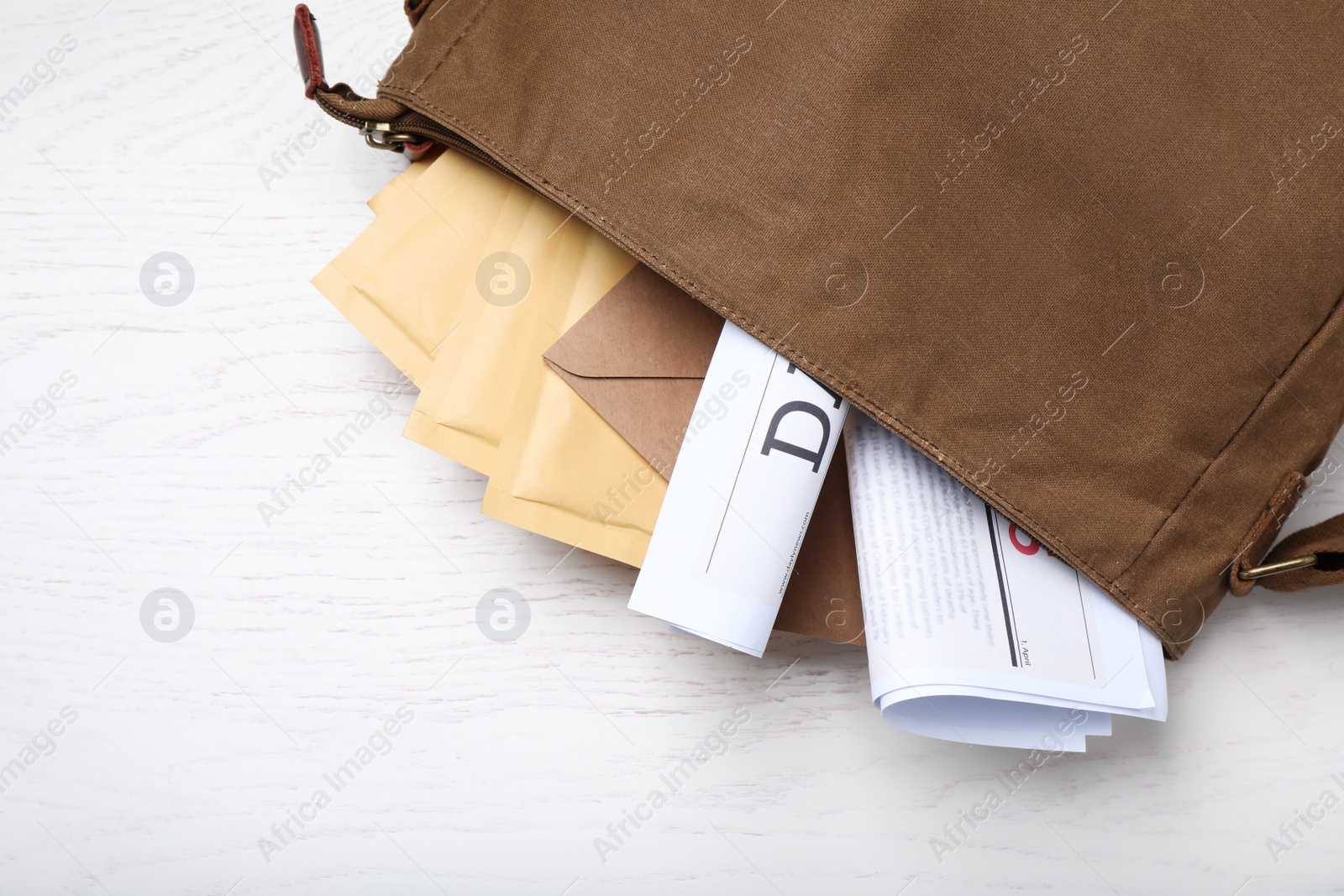Photo of Brown postman's bag with envelopes and newspapers on white wooden table, top view. Space for text