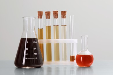 Photo of Different laboratory glassware with brown liquids on table against light background