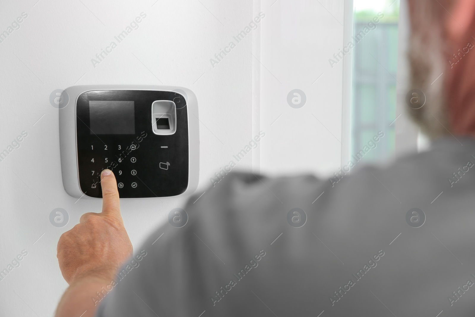 Photo of Mature man entering code on alarm system keypad indoors